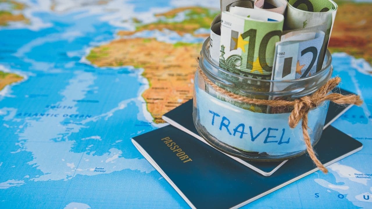  A jar filled with money labelled 'travel' sits on top of a passport on a world map, representing the search query 'Budgetfriendly travel destinations with low cost of living'.