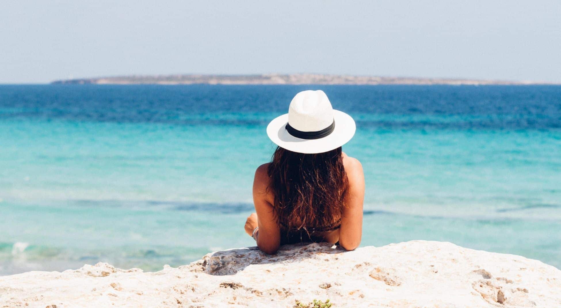 woman in white hat looking at the ocean on vacation