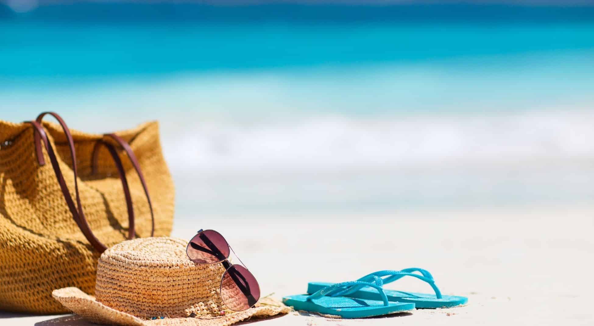shot of hat, glasses, beach bag, and sandals on the sand