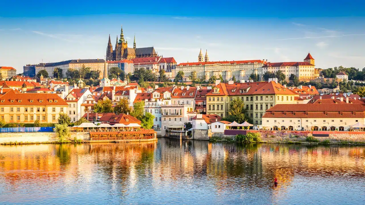 waterfront view of Prague's iconic red roofs and castle spires