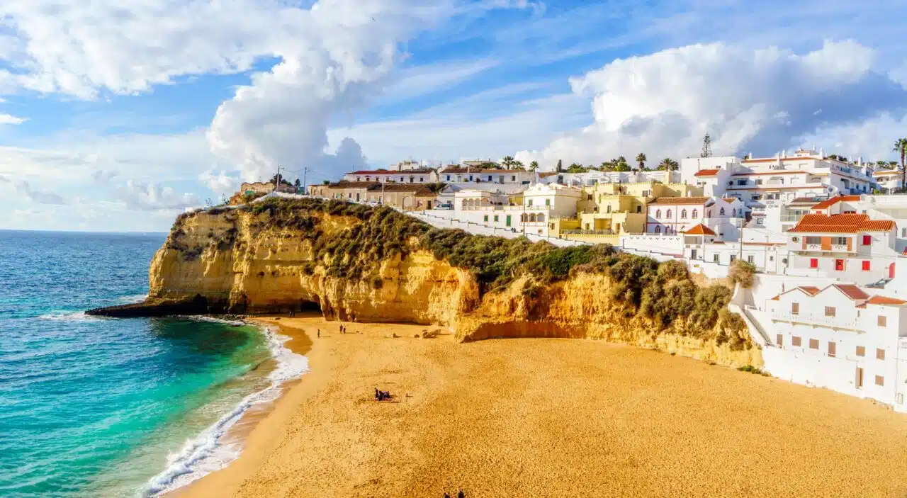 Golden sand beach backed by white buildings and surrounded by turquoise blue waters and rocky cliffs 