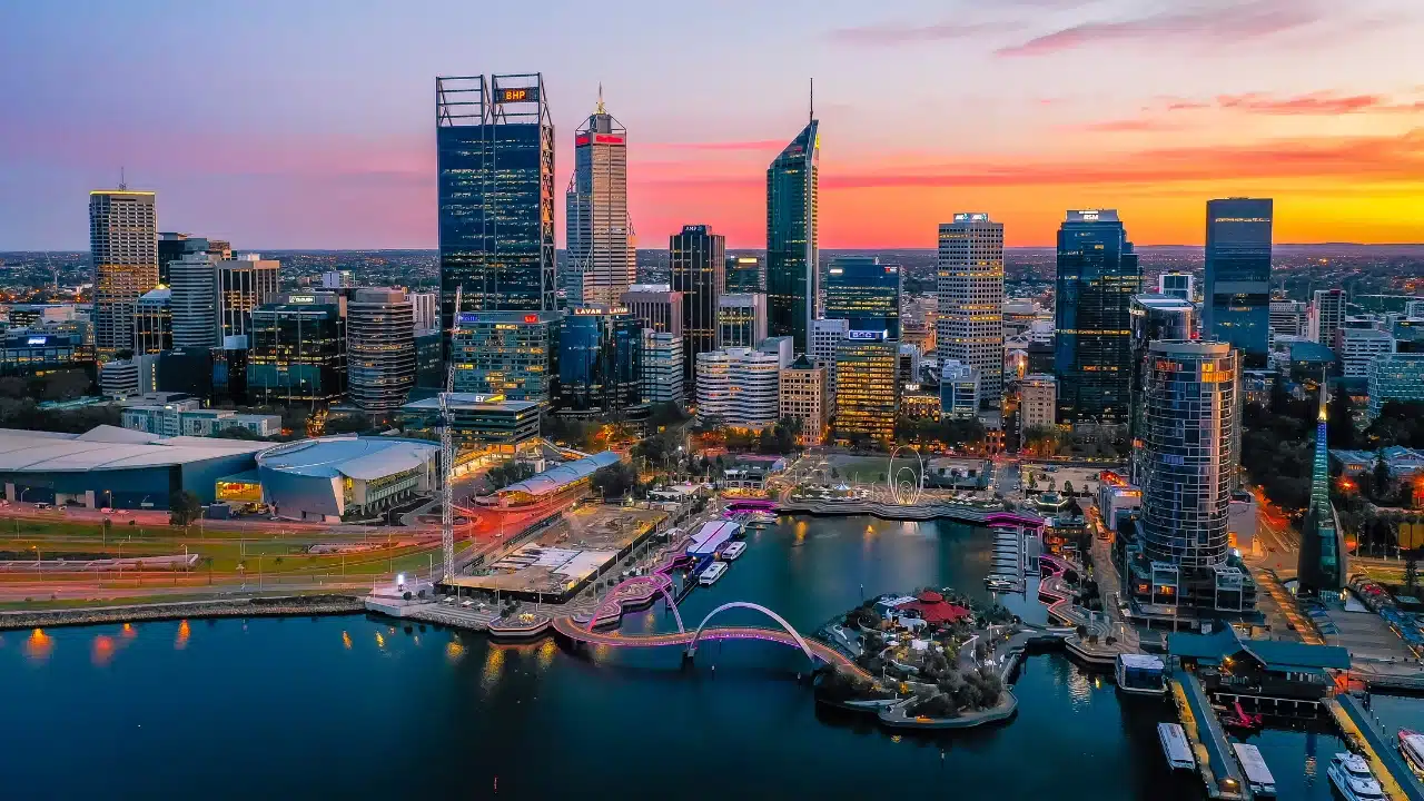 Perth skyline at sunset overlooking Elizabeth Quay in Western Australia, featuring modern skyscrapers, waterfront attractions, and vibrant city lights along the Swan River.