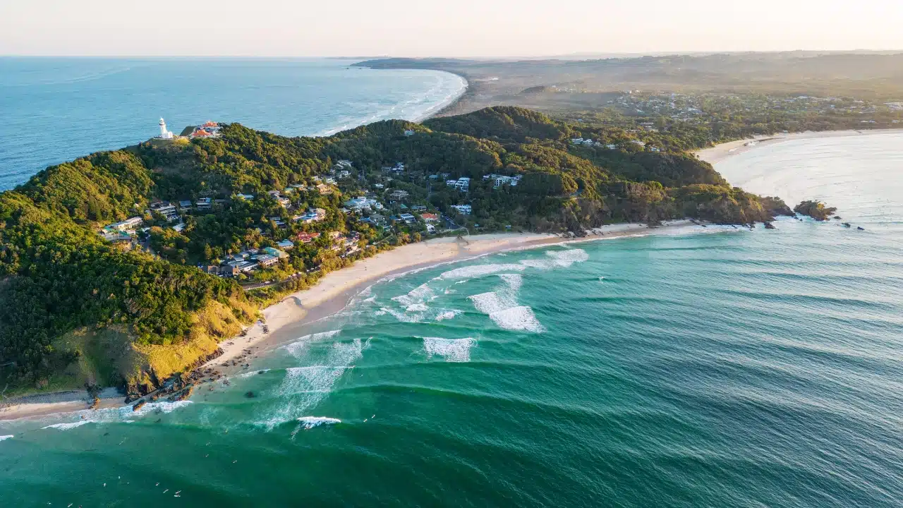 Aerial view of Byron Bay, Australia, featuring Cape Byron Lighthouse, lush coastal hills, sandy beaches, and turquoise waters along the New South Wales coast.