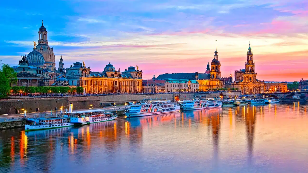 Panoramic view of Dresden, Germany, featuring the historic Old Town, Frauenkirche, Elbe River, riverside architecture, and boats at sunset.