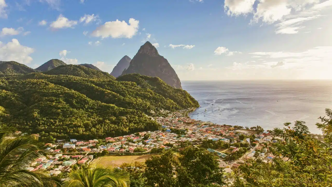 Panoramic view of Saint Lucia's Pitons overlooking Soufrière, a lush coastal town surrounded by tropical hills and the Caribbean Sea.